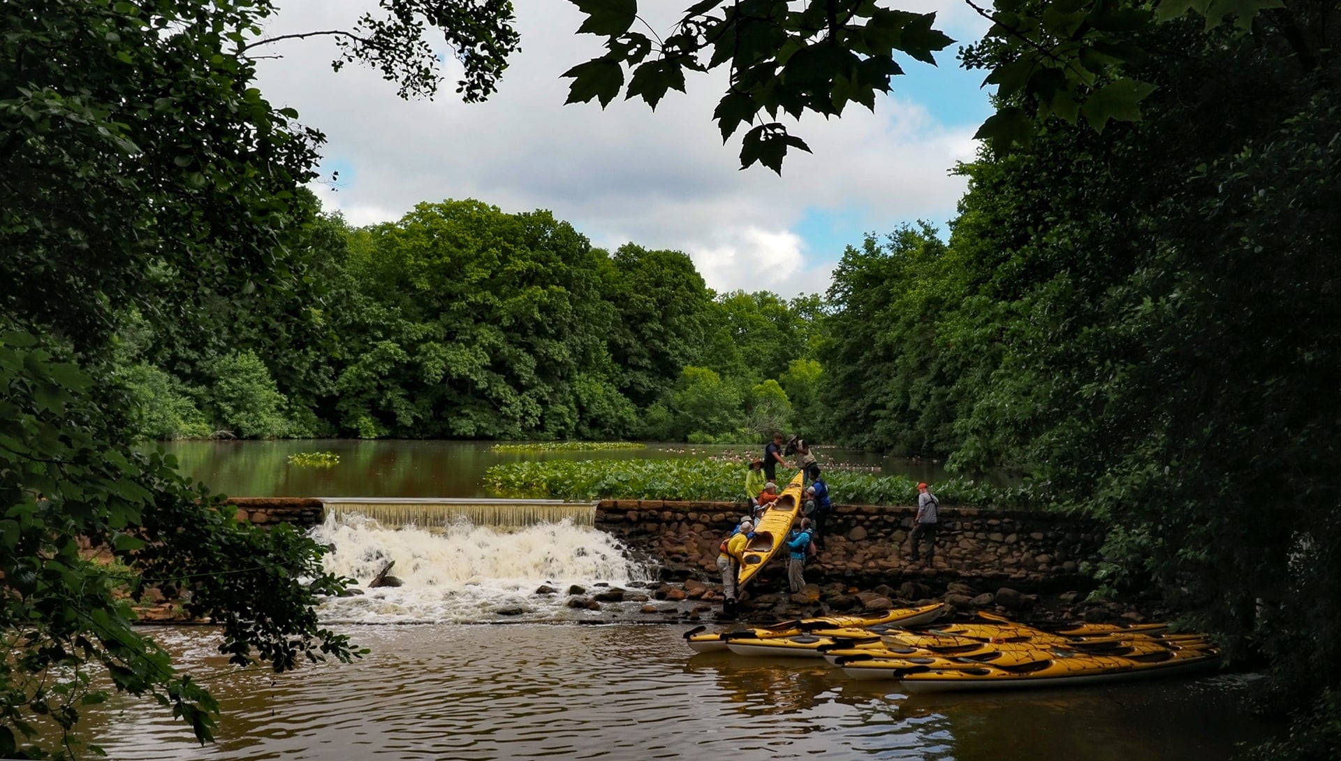 Kayakers launching below a stone dam on the river